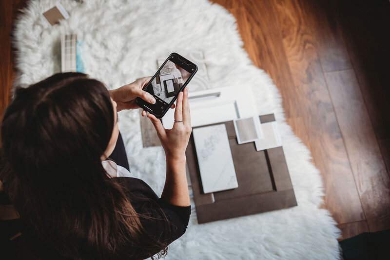 Woman taking a photo from above of interior design samples on the floor for a plat lay photo.