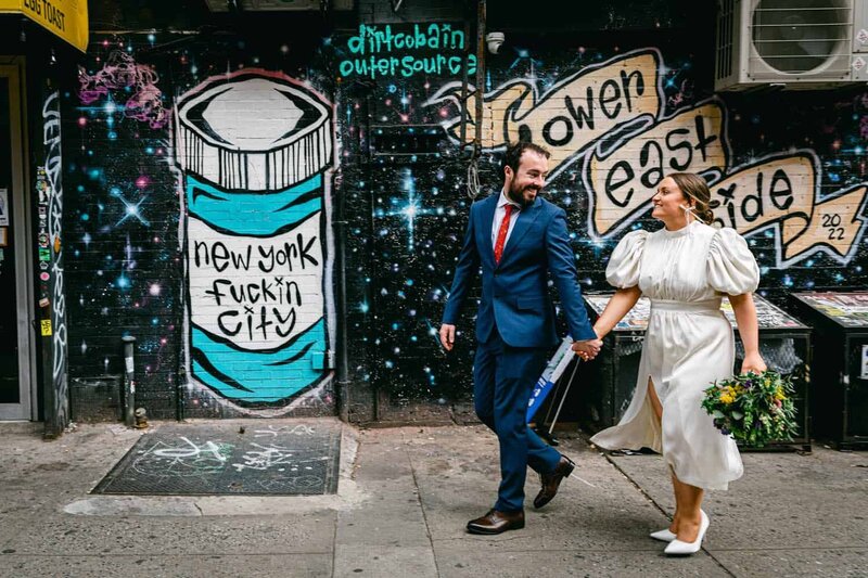 A couple jump in the air at a colorful mural in DUMBO