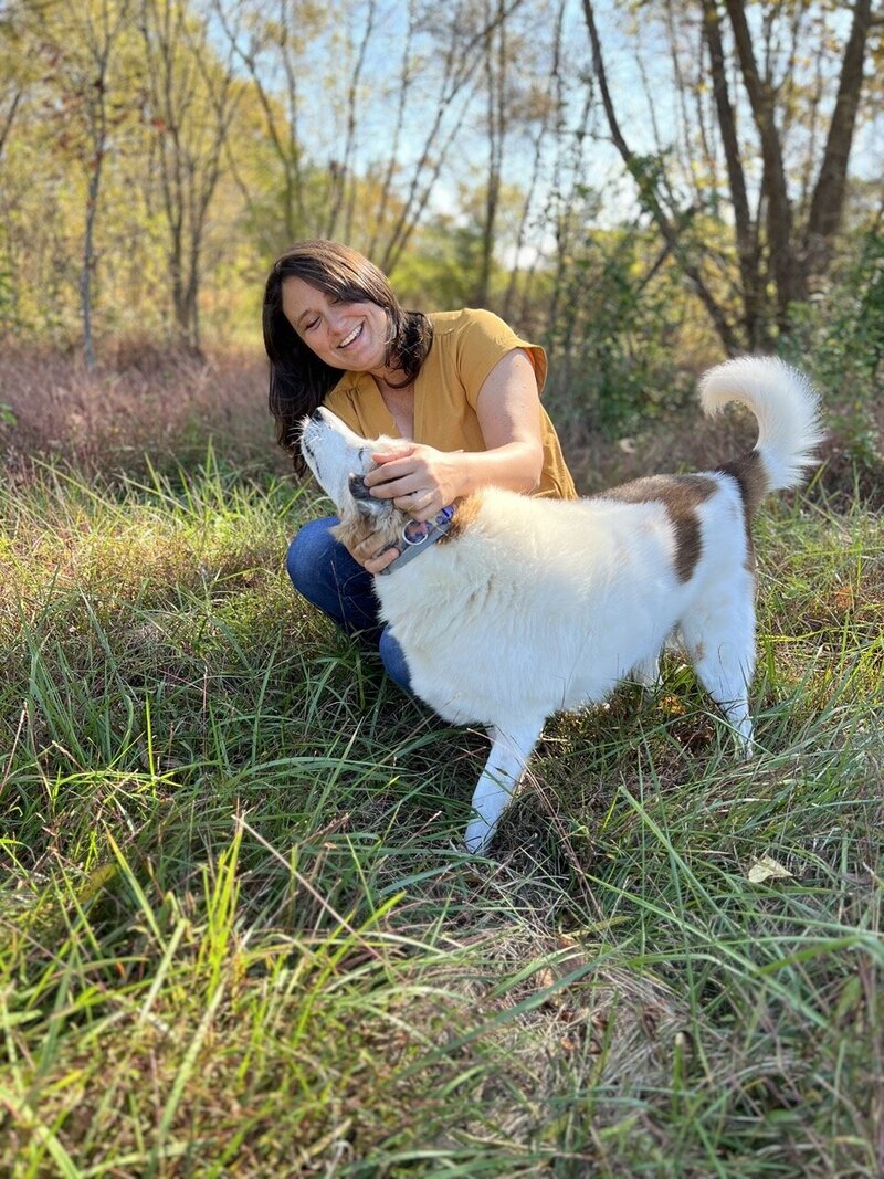 The owner of Nashville Family Films & Photo squats in a field with her dog for a photo.