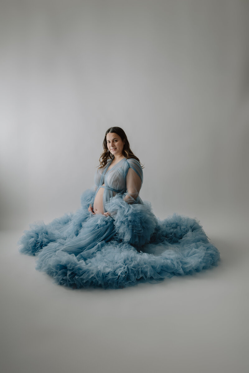 Glamour shot of pregnant mom in blue fluffy robe with white background in studio in Severn Maryland..