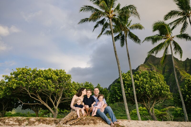 A family of five sit on the edge of a beach at Kualoa regional park.