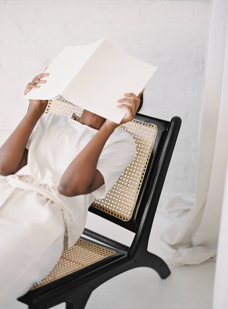 woman sitting in chair with book over her head