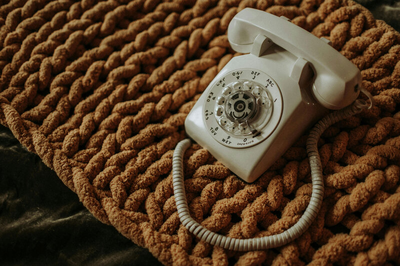 Old, white rotary phone sitting on a crochet covered bench