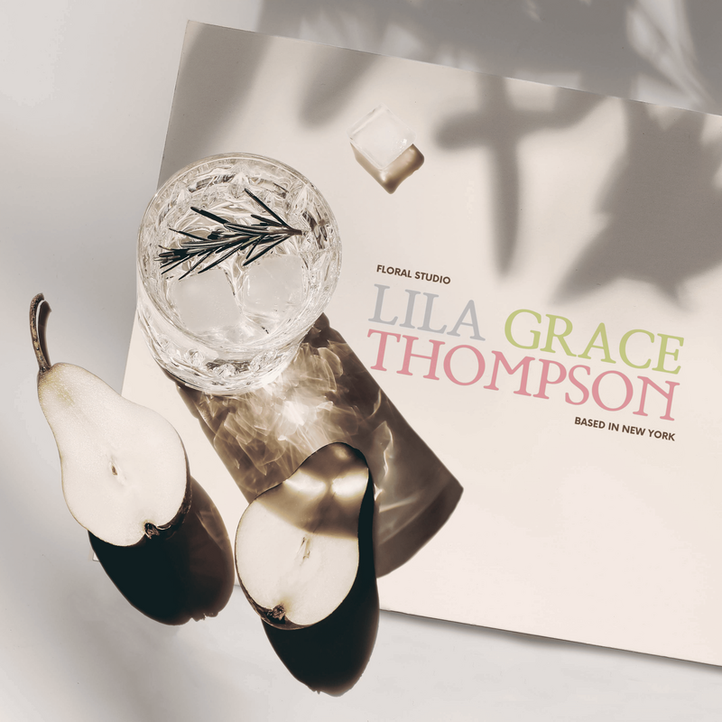 A branding mockup featuring a glass of water with rosemary, two pears, and a card with the Lila Grace Thompson Floral Studio logo and the text "Based in New York." The image is styled with soft lighting and subtle shadows.