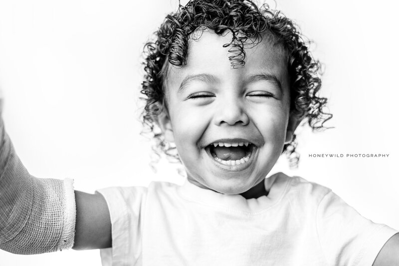Black and white portrait of a joyful child with curly hair laughing, captured during a personality photography session in Grand Rapids, Michigan