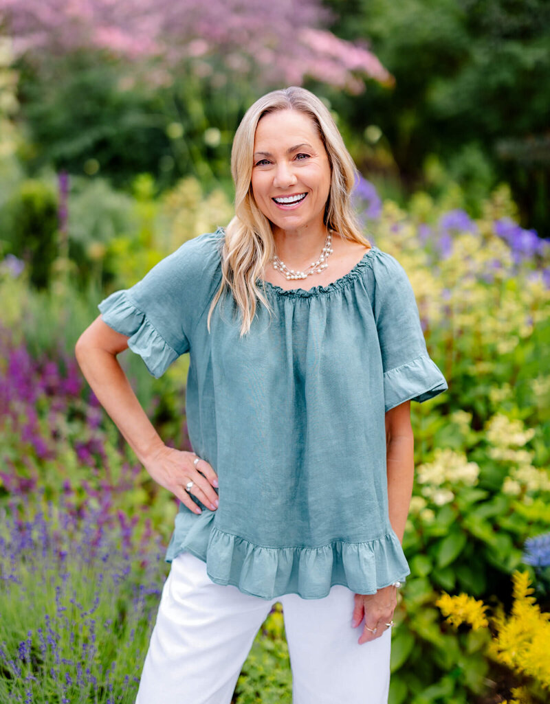 An image of Alison Smiley, a Seattle Bar and Bat Mitzvah photographer in a blue shirt standing in a garden