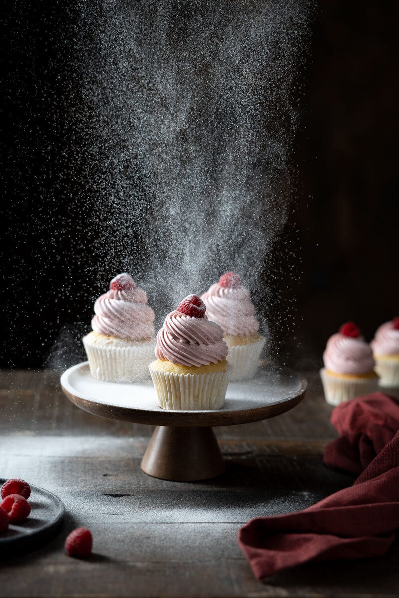 Actie food fotografie in Studio X34. Poedersuiker valt op roze cupcakes met frambozen. Food fotografie door Dorien Paymans | Studio Ensō Groningen ©