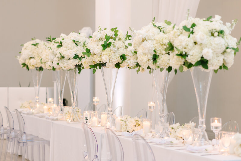 translucent vases with white flowers adorn a wedding reception table