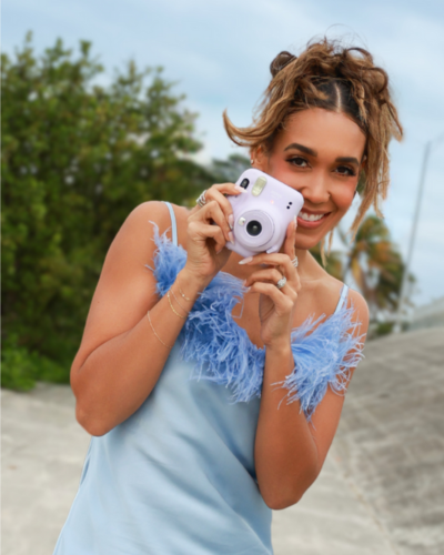 Host Simone Boyce in blue dress taking a picture with a polaroid camera
