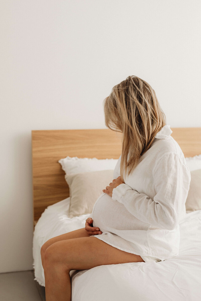 Pregnant woman sitting at the edge of a bed