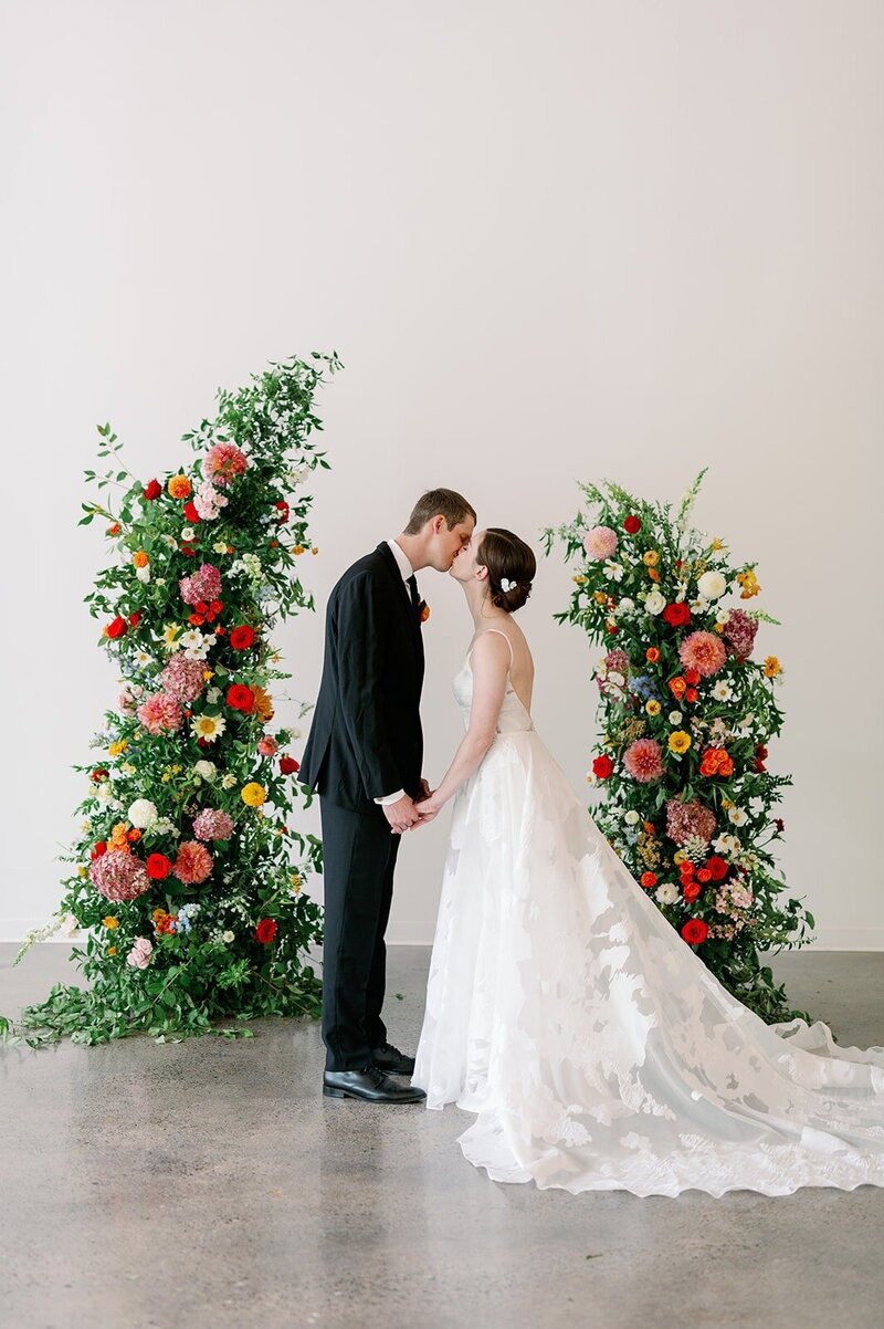 bride and groom kiss near colorful floral partial arch design for minneapolis wedding photographed by bauer creative