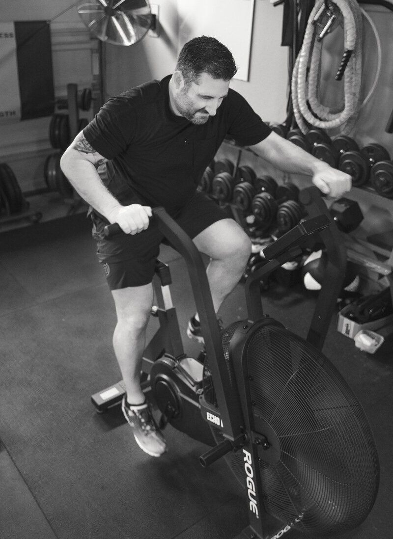 Man is on an airbike at Silverback Fitness during a personal training session. He is actively working out and being trained by the best personal trainer in Sarnia, ON Jim Stewart.