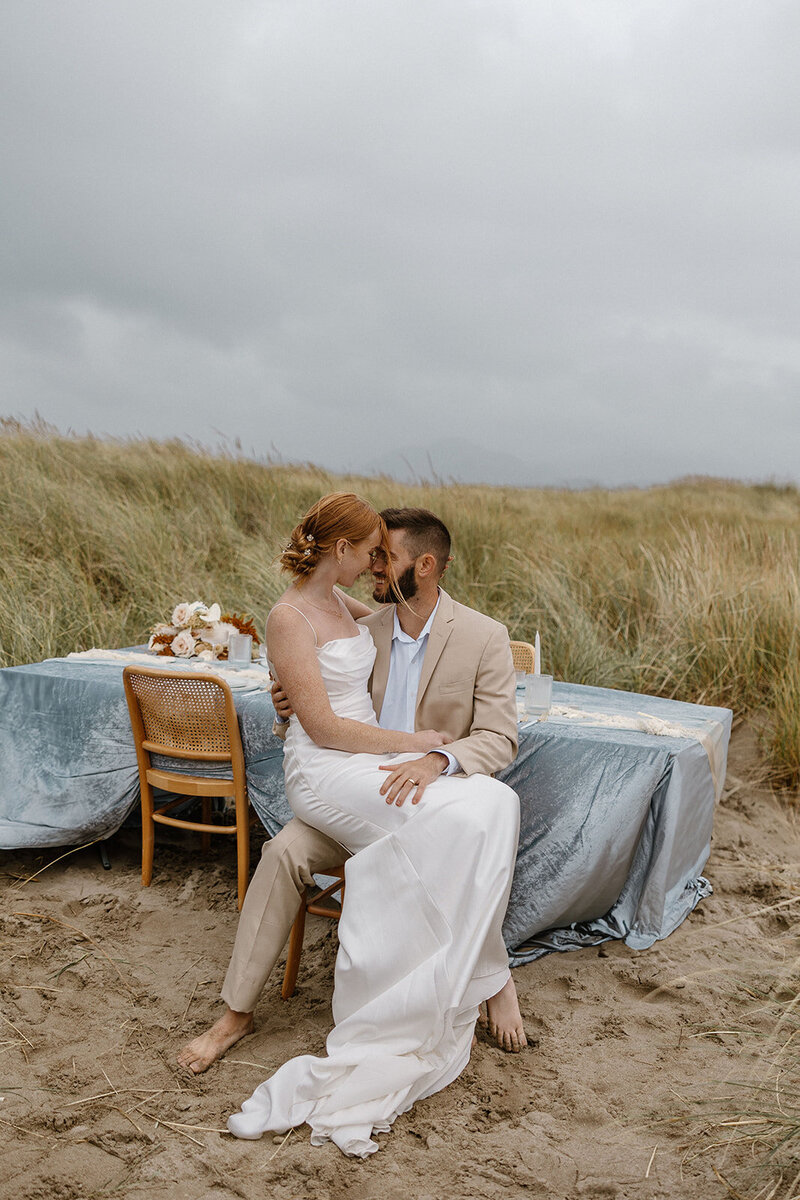 Bride sits in her grooms lap during their private dinner on the oregon coast.