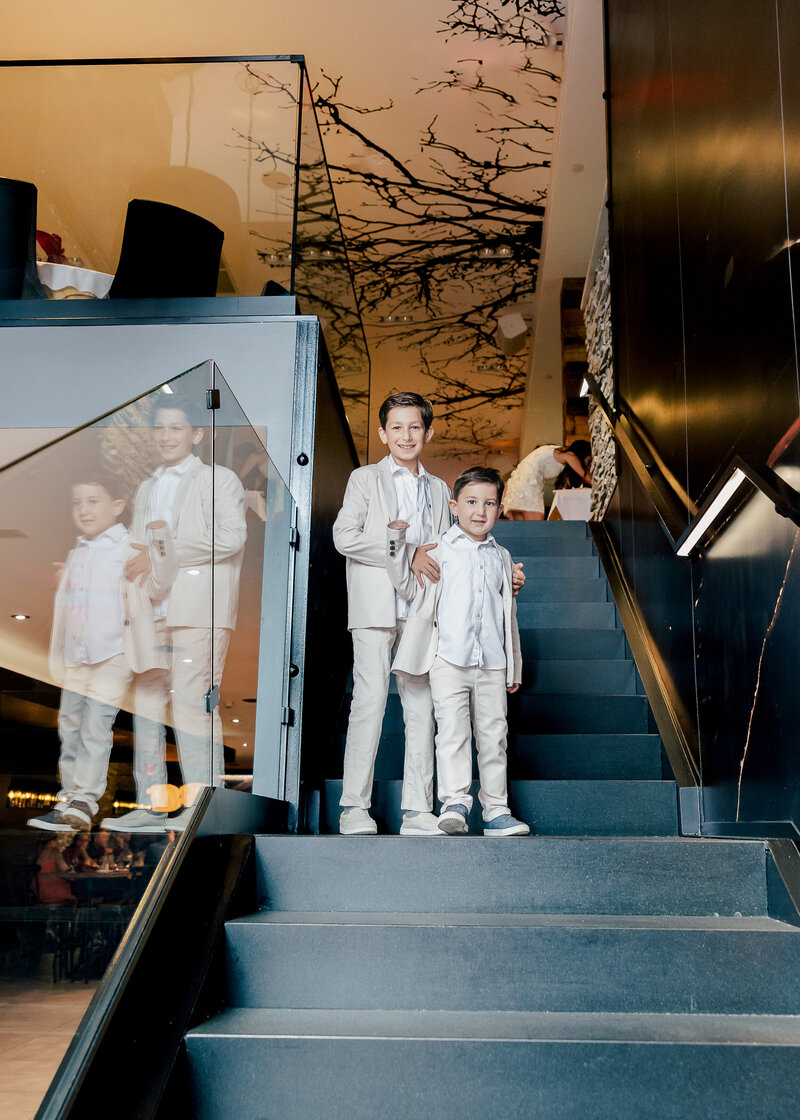 Posed portrait of young brothers in white suits on stairs at a formal birthday party.