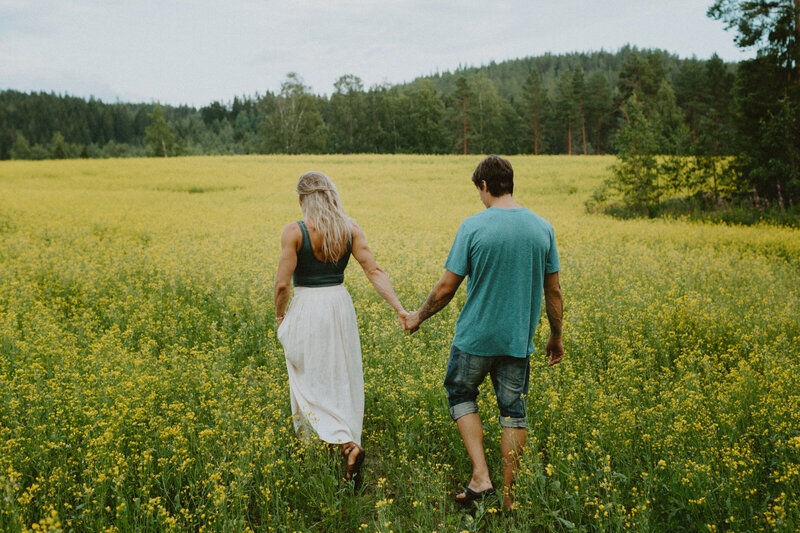 Engaged couple walking hand in hand in a rapeseed field in Finland