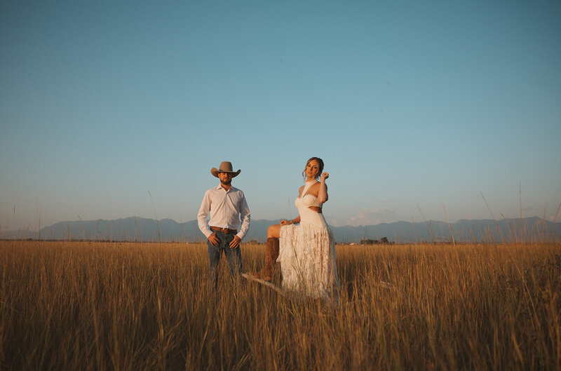 couple in a wide open grassy field wearing western cowboy hat and boots with mountains in the distance