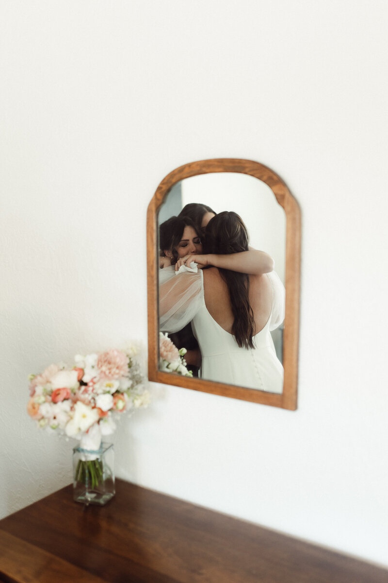 Mirror photo of bride hugging the mother of the bride before she walks down the isle. 