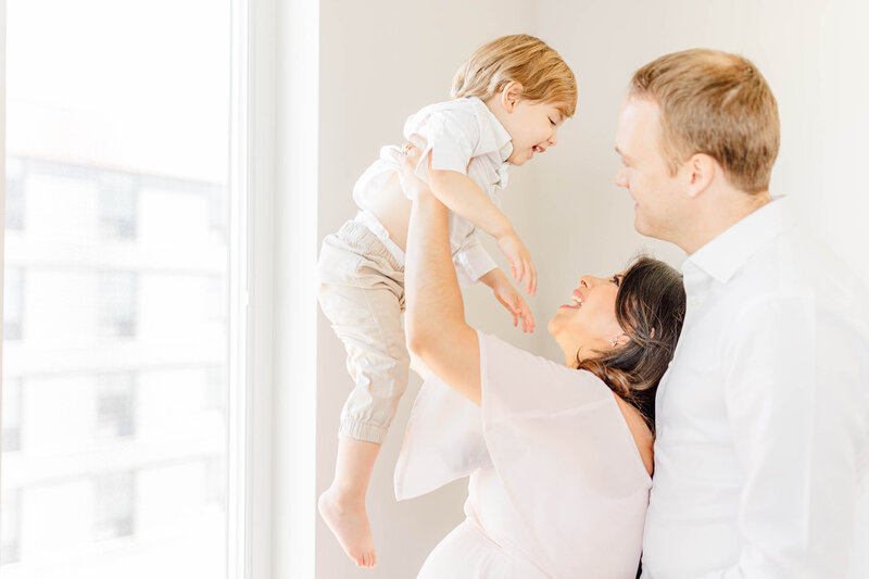 Pregnant mom holds up laughing child as father looks on