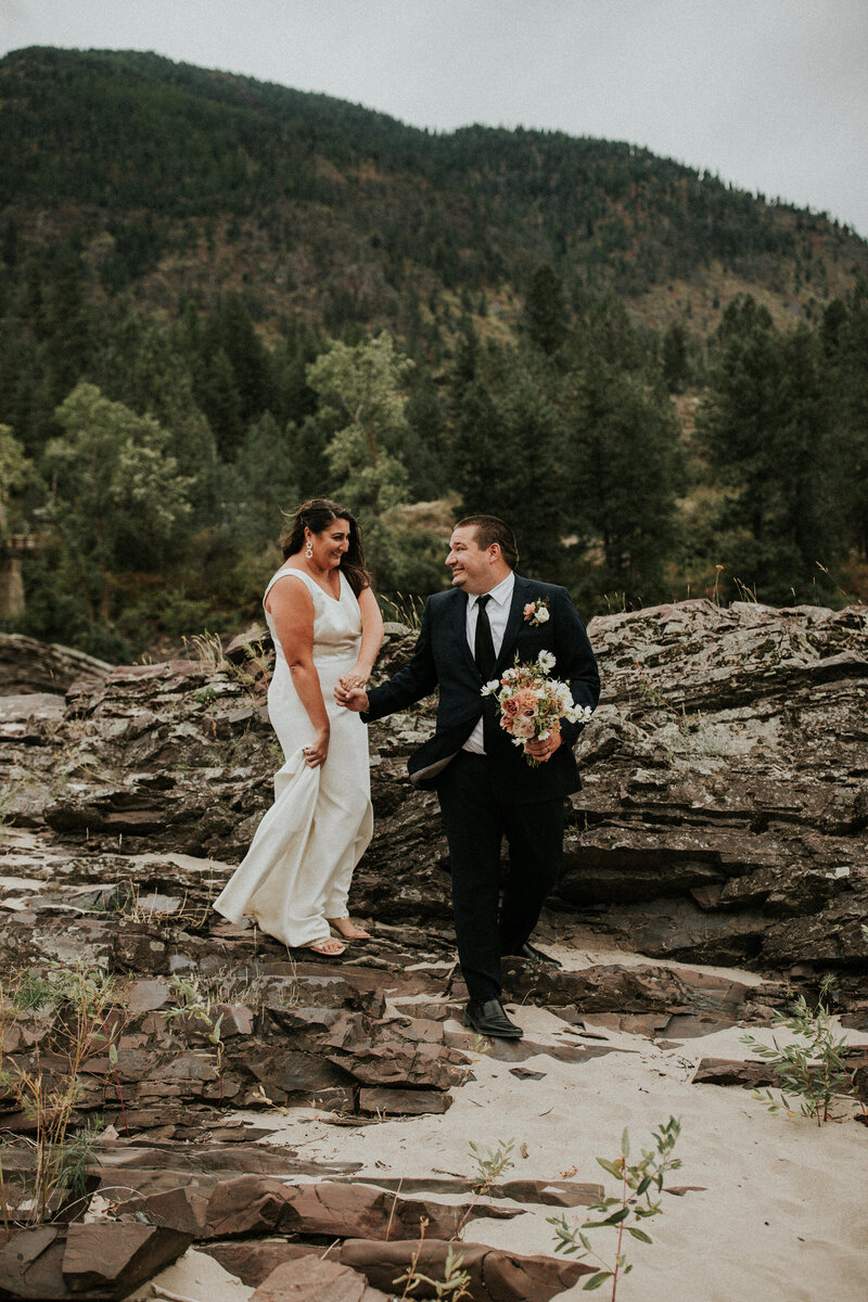 A groom helps his bride step down from a rock by holding her hand