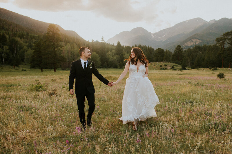 couple holding hands on their wedding day running through a field in rocky mountain national park