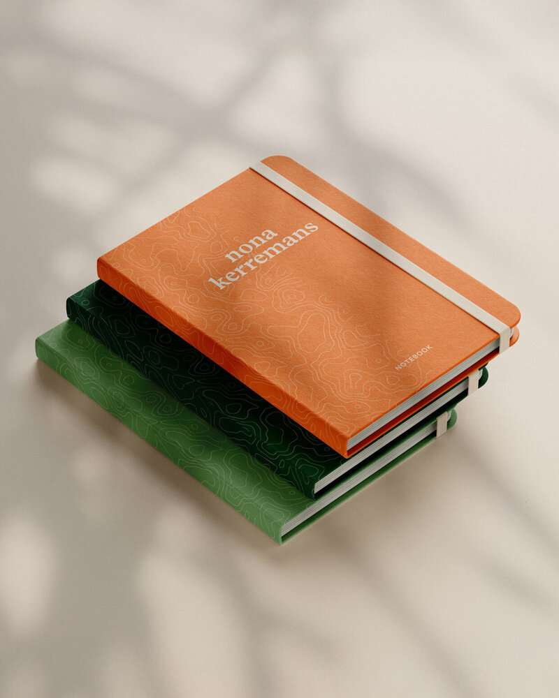 Oranje en groene notitieboeken met topografisch patroon en logo van Nona Kerremans, ontworpen als onderdeel van een complete huisstijl door Studio Vers.