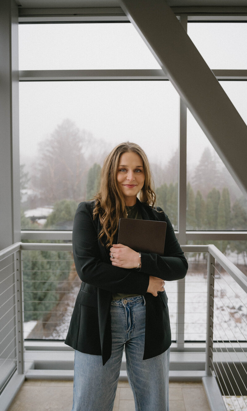 Girl with brown hair holding laptop and smiling at camera