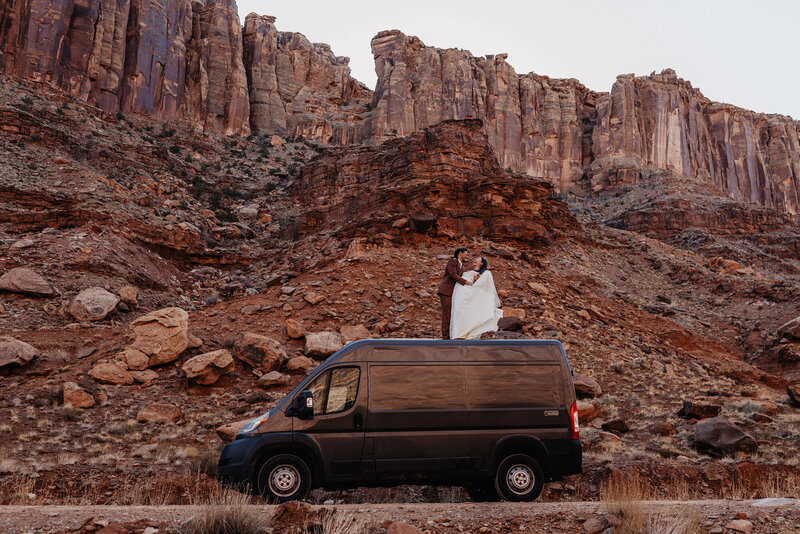 Bride and groom standing on top of van in wedding clothes