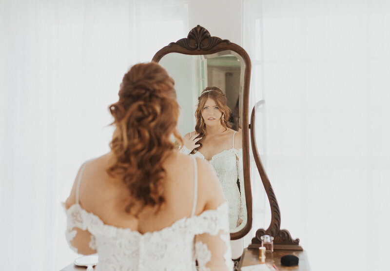 Bride in wedding gown standing in front of a mirror in the bridal suite