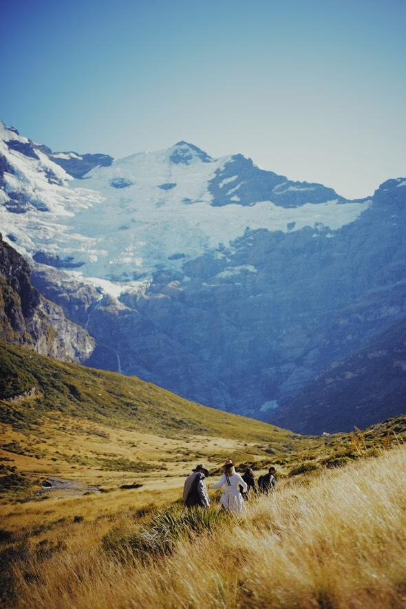 A group being lead through tussocky ground underneath a glacier mountain.