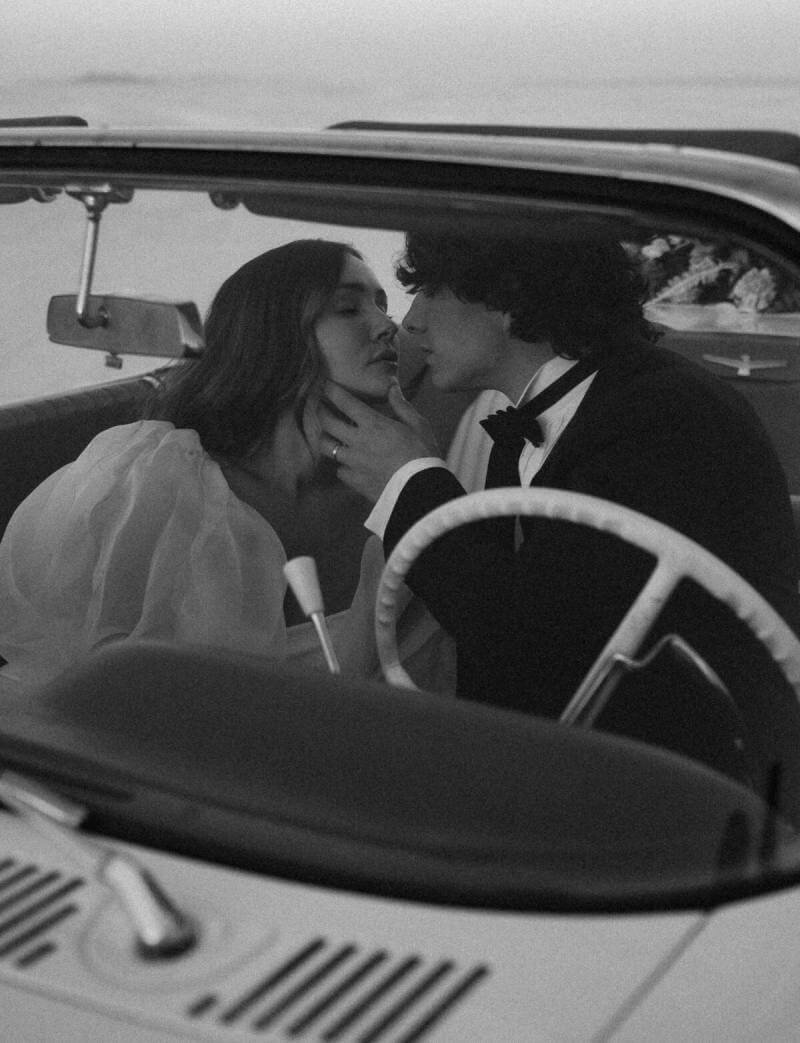 Romantic black and white wedding photo of a bride and groom in a vintage car.