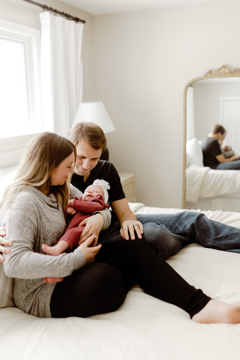 Mom and dad are cuddling the baby on the bed