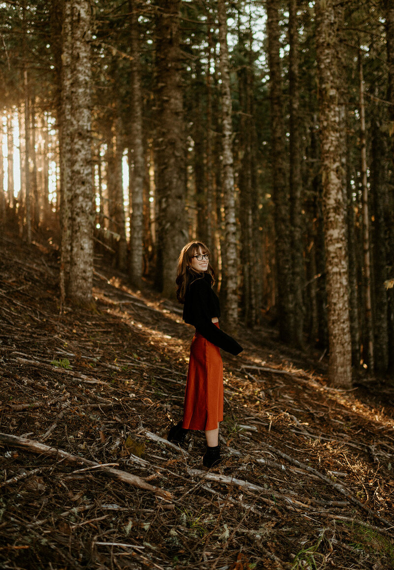 girl in red skirt and black sweater standing on hill in the forest