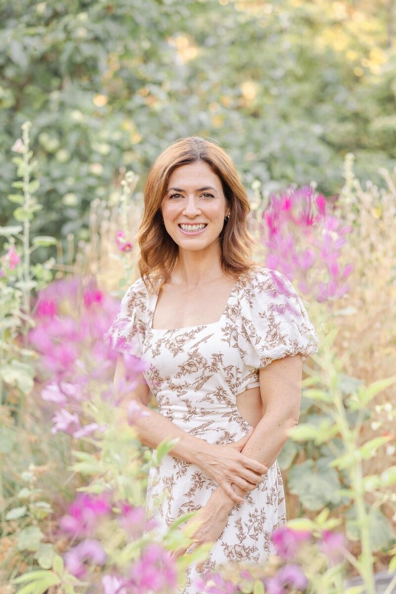 Woman in her 30s standing outside and looking back over her shoulder smiling at the camera