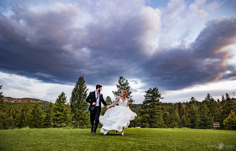 Couple Hold Hands as they run across the lawn at The Woodlands Wedding Barn in Colorado