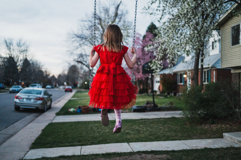 Child in a red dress swinging outside at dusk, captured during a documentary-style family photography session