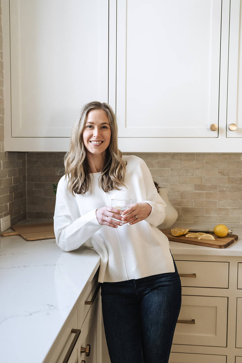 Erica Taylor smiling in her kitchen with a glass of lemon water—introducing free wellness tools to help moms boost energy and simplify nutrition