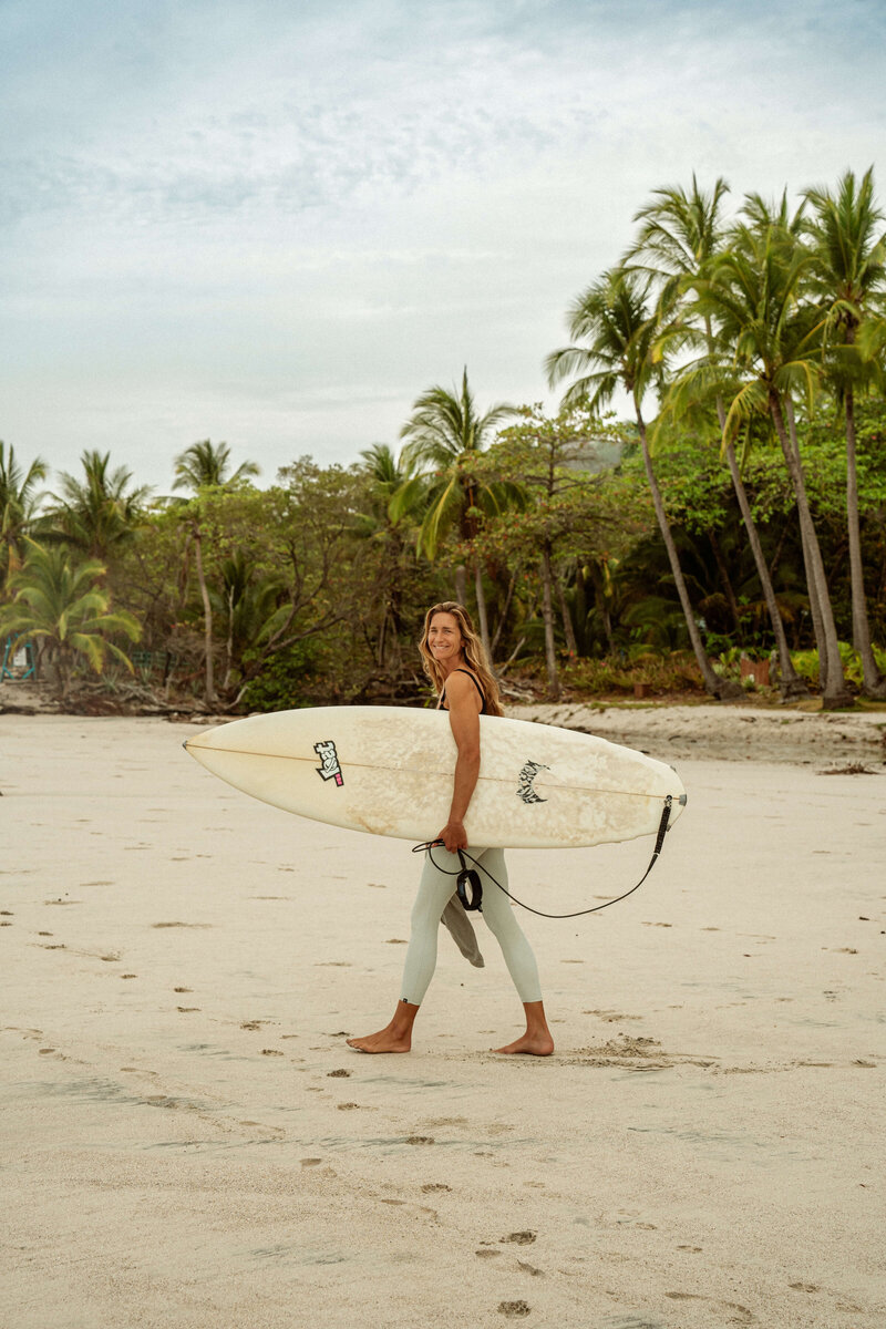 Woman walking on beach holding surfboard