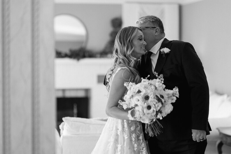 The father of the bride has a first look with his daughter. The photo is in black and white. The dad has a gentle touch of his hand on the brides arm. 
