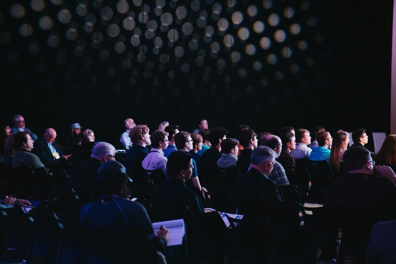 Rear side view of an audience listening to a presentation in a dark room