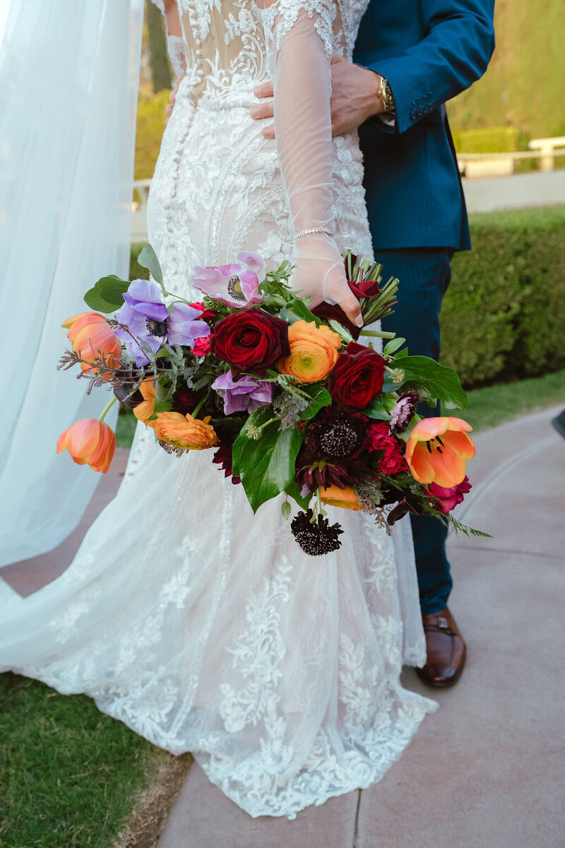 A stunning bouquet of colorful flowers held by a bride with his groom.