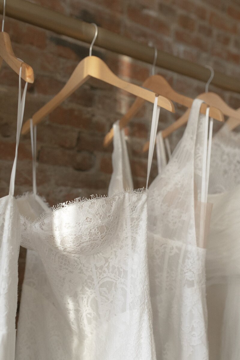 Close-up of lace wedding dresses hanging on wooden hangers.
