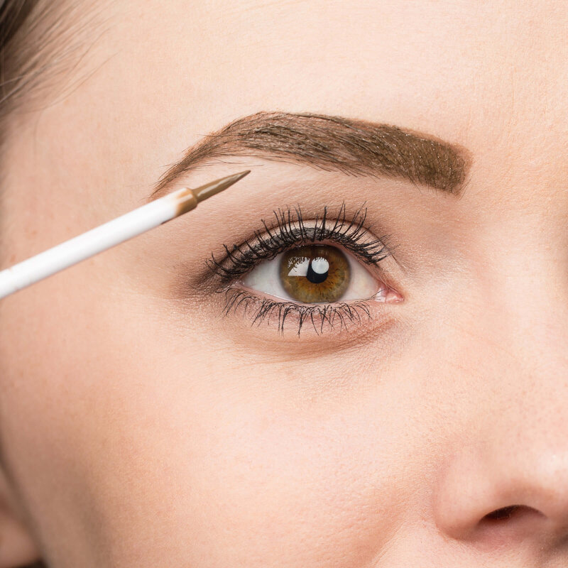 Close-up of woman's eye and brow as she applies makeup.