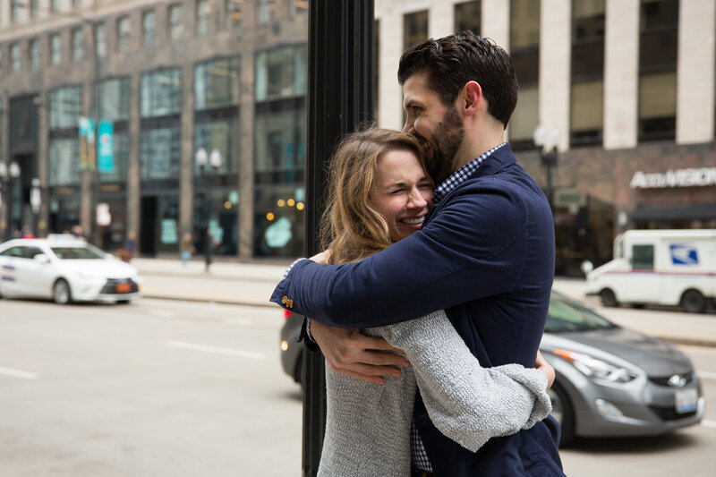 couple hugging after surprise proposal woman gasping from surprise engagement downtown chicago mag mile