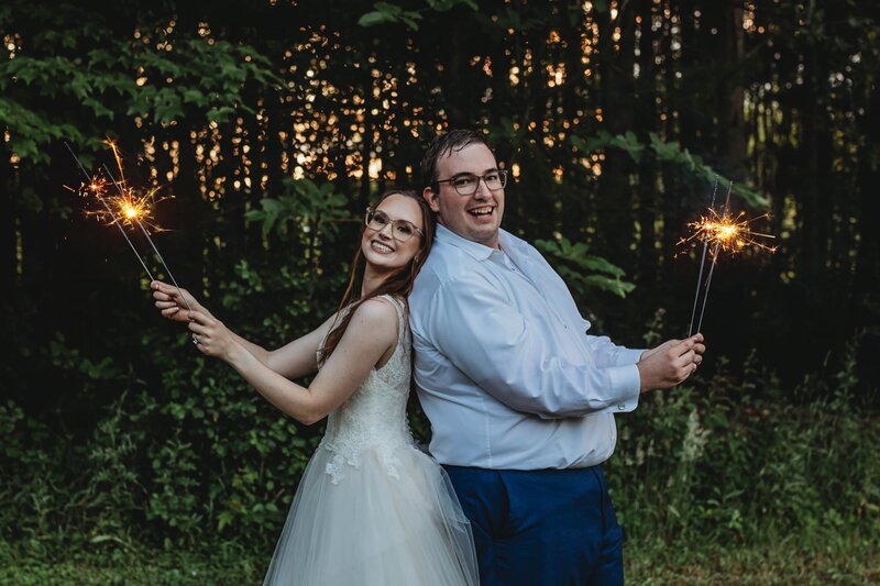 bride and groom standing back to back holding sparklers