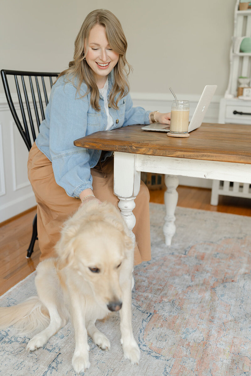 Woman bending over to the side of the table to pet an english-cream golden retriever on the back