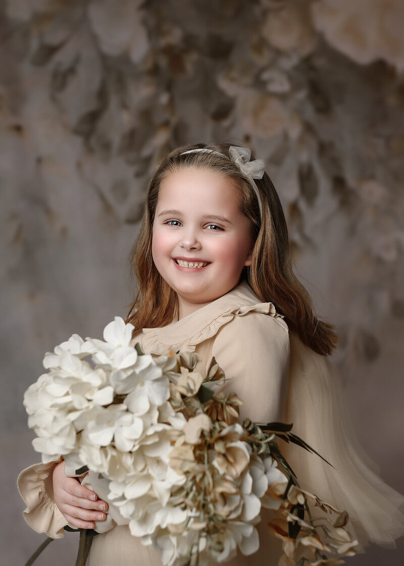 6 year old girl holding flowers standing  with a floral backdrop