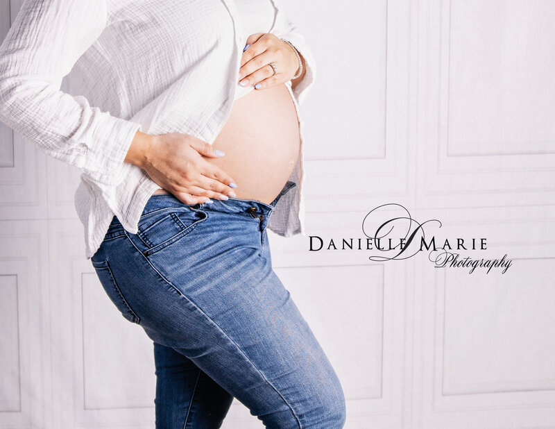 Young mom posing with a white shirt and jeans holding her baby bump in New Jersey 