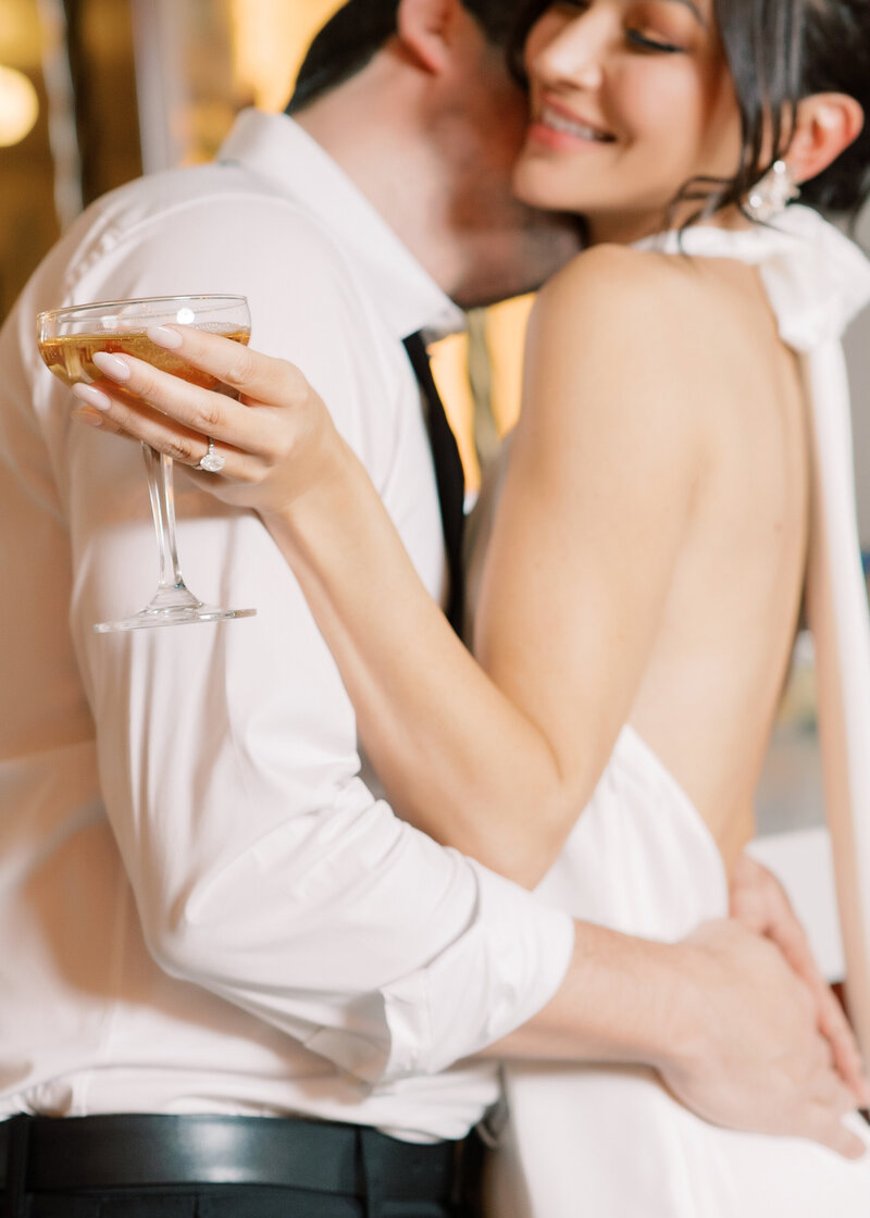 A photo taken during a wedding. Couple embraces over a glass of champagne.