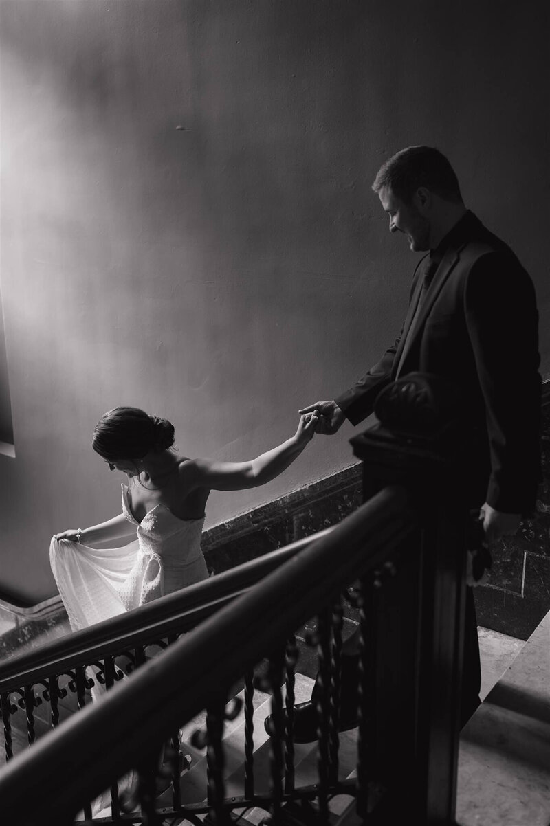 Bride leads groom down the stairs of elegant stairwell