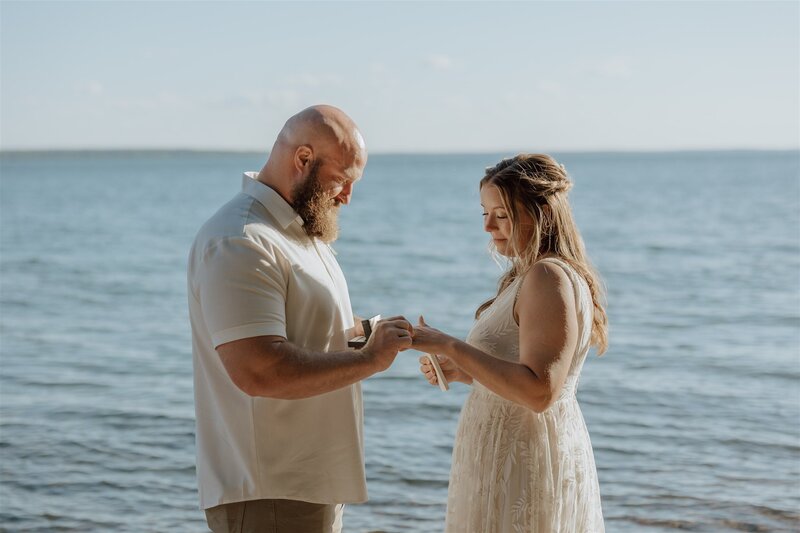 bride and groom exchanging rings during their elopement ceremony on hermit island with lake superior in the background